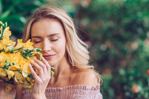 Mujer joven rubia cerrando los ojos tocando las flores de fresia