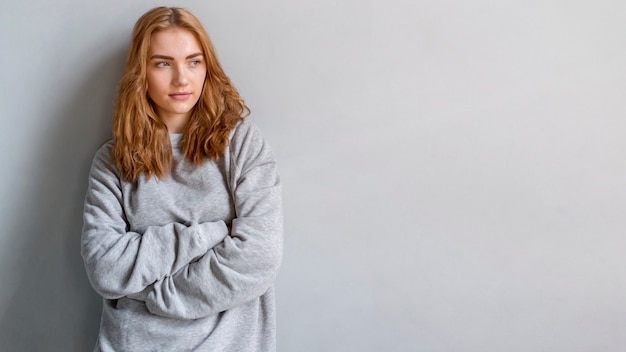 Mujer joven rubia contra la pared gris que mira lejos