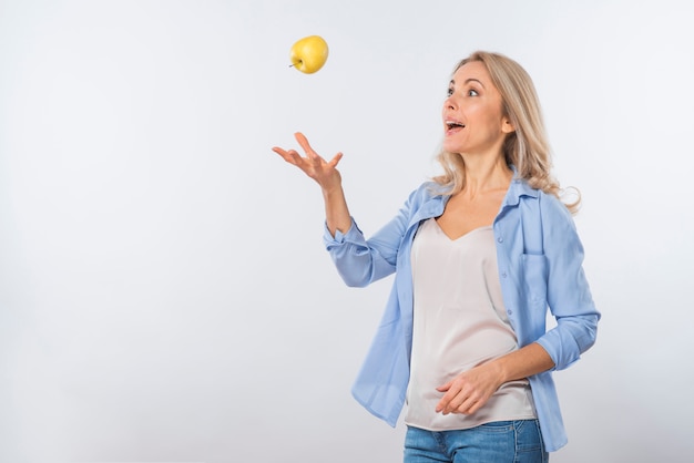 Foto gratuita mujer joven rubia emocionada que lanza la manzana en el aire contra el contexto blanco