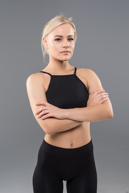 Mujer joven rubia en forma deportiva chica en ropa deportiva negra demuestra su fuerte cuerpo musculoso estiramiento