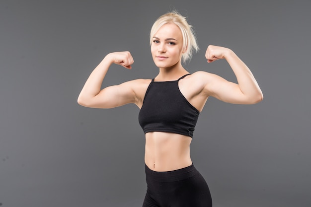 Mujer joven rubia en forma deportiva chica en ropa deportiva negra demuestra su fuerte cuerpo musculoso estiramiento