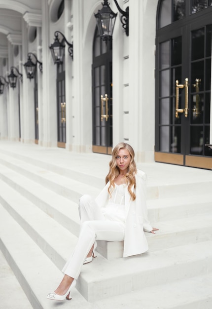 Foto gratuita mujer joven rubia de pelo rizado en traje blanco de estilo clásico sentado posando en las escaleras chica modelo de novia caucásica hermosa en ropa de moda de boda estilo de boda