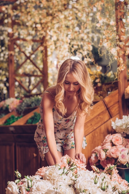 Foto gratuita mujer joven rubia que arregla las rosas en el jardín de flores