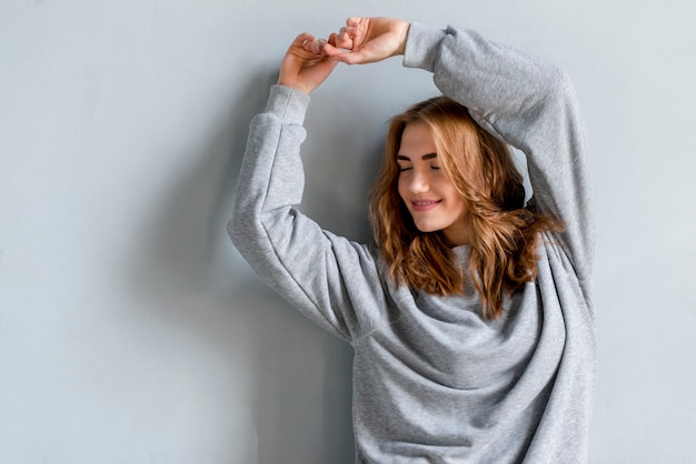 Mujer joven rubia que baila delante de la pared gris