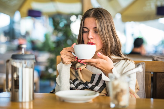 Mujer joven rubia que bebe té herbario en la taza blanca