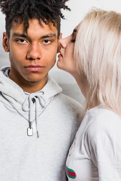 Mujer joven rubia que besa a su novio africano serio en su mejilla