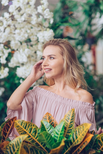 Foto gratuita mujer joven rubia que se coloca delante de la planta del croton del jardín