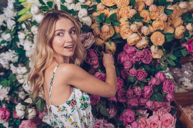 Foto gratuita mujer joven rubia que se coloca delante de las rosas que miran lejos