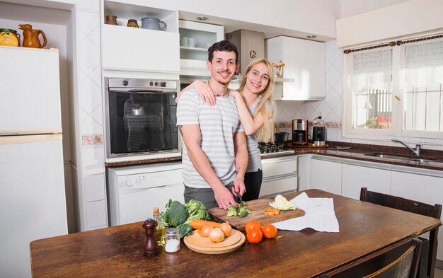 Mujer joven rubia que se coloca con sus verduras del corte del marido en la cocina