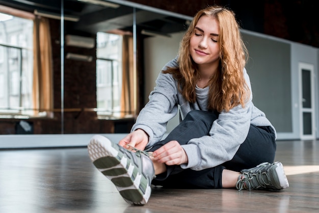 Mujer joven rubia que se sienta en el piso que ata el cordón