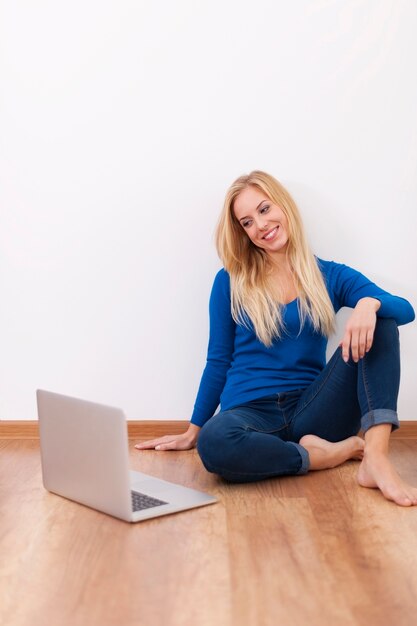 Mujer joven rubia sentada en el piso de madera con laptop