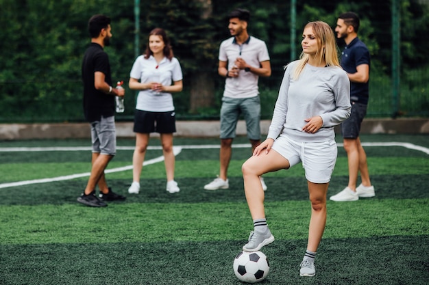 Mujer joven, rubia, sonriente y feliz, con balón de fútbol, emocionada de jugar un juego