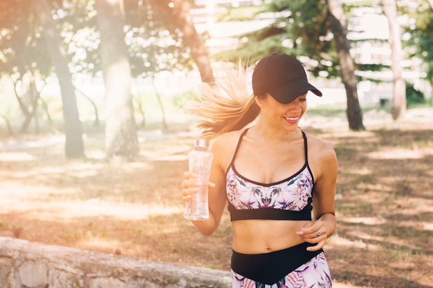 Foto gratuita mujer joven rubia sonriente que sostiene la botella de agua disponible