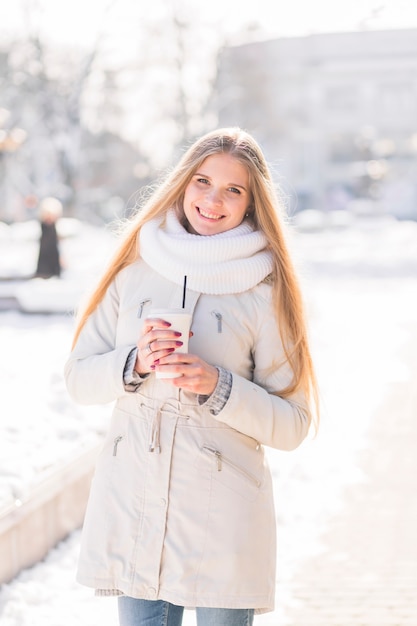 Mujer joven rubia sonriente que sostiene la taza de café disponible en invierno