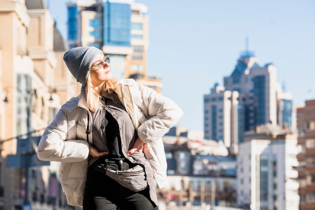 Mujer joven rubia con sus manos en las caderas que se colocan delante de la presentación del horizonte de la ciudad