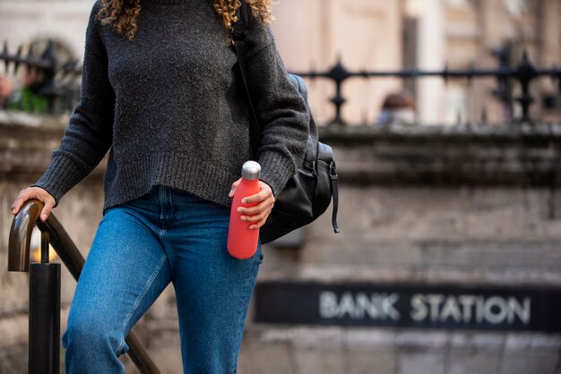 Mujer joven saliendo del metro y sosteniendo una botella de agua en la ciudad