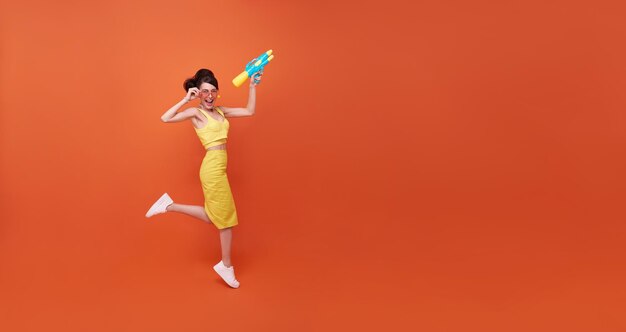 Mujer joven saltando belleza feliz con pistola de agua y durante el estudio del festival Songkran filmada en el espacio de copia fondo naranja