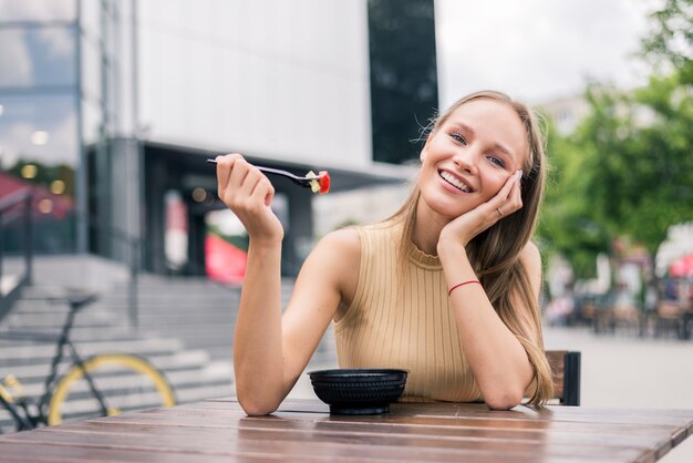 Mujer joven sana comiendo ensalada al aire libre en la cafetería de la calle