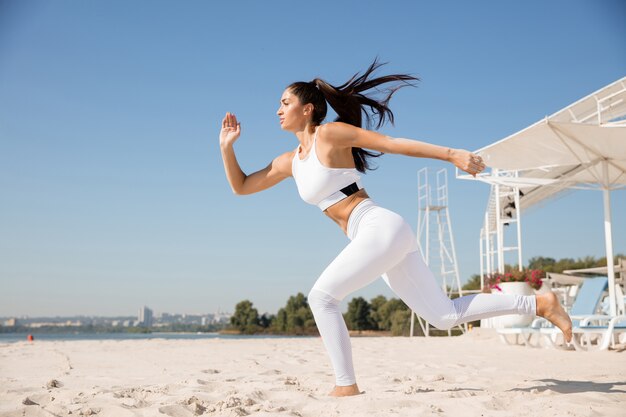 Mujer joven sana corriendo y haciendo estocadas en la playa.