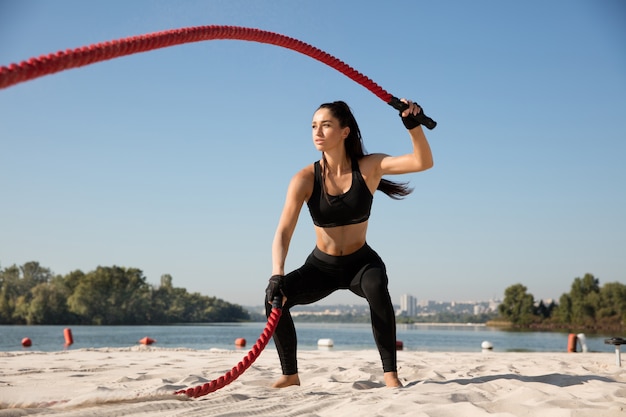 Mujer joven sana haciendo ejercicio con las cuerdas en la playa.