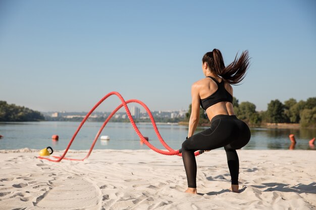 Mujer joven sana haciendo ejercicio con las cuerdas en la playa.