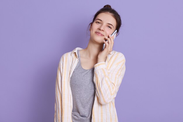 Mujer joven satisfecha hablando por teléfono inteligente moderno