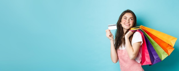 Foto gratuita mujer joven satisfecha sonriendo mostrando tarjeta de crédito de plástico y sosteniendo bolsas de compras comprando con cont.