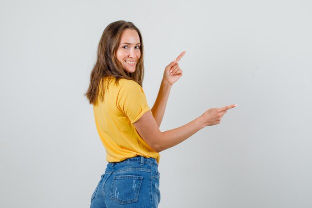 Mujer joven señalando con el dedo y sonriendo en camiseta, pantalones cortos.