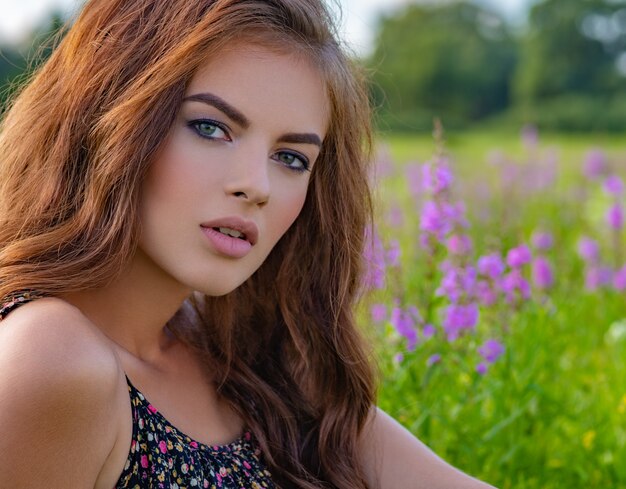 Mujer joven sentada al aire libre en un campo de flores de color púrpura. Modelo posando en flores de lavanda.