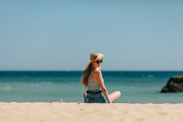 Mujer joven sentada en la arena y mirando al mar. Vista trasera