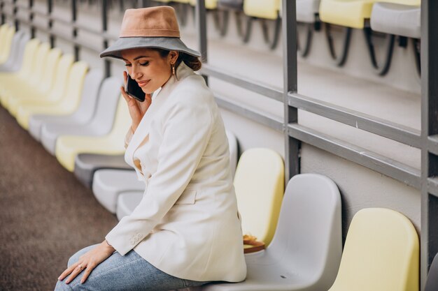 Mujer joven sentada en los asientos de la arena y hablando por teléfono