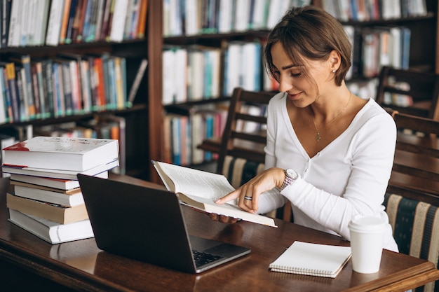 Mujer joven sentada en la biblioteca con libros y computadora