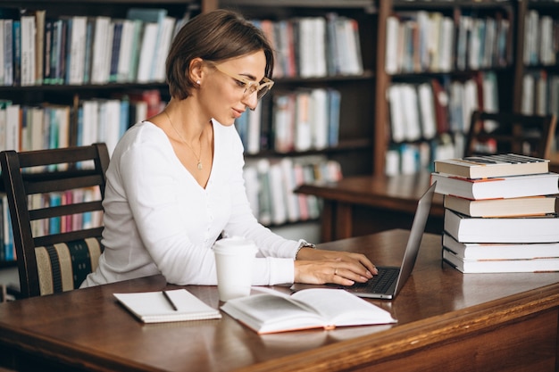 Mujer joven sentada en la biblioteca con libros y computadora