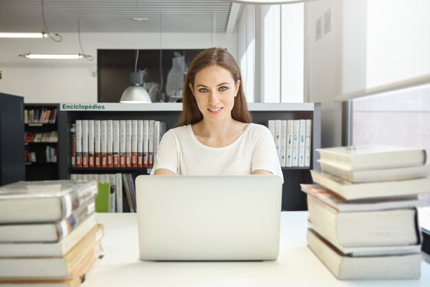 Mujer joven sentada en la biblioteca con un portátil