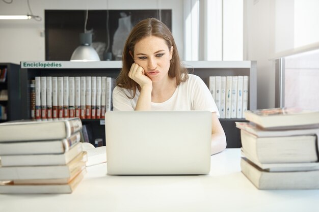 Mujer joven sentada en la biblioteca con un portátil