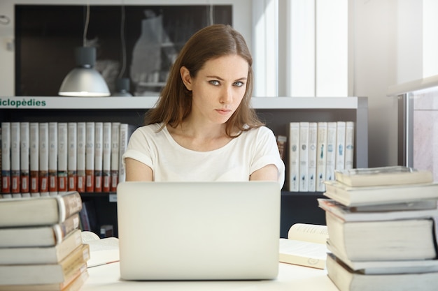 Mujer joven sentada en la biblioteca con un portátil