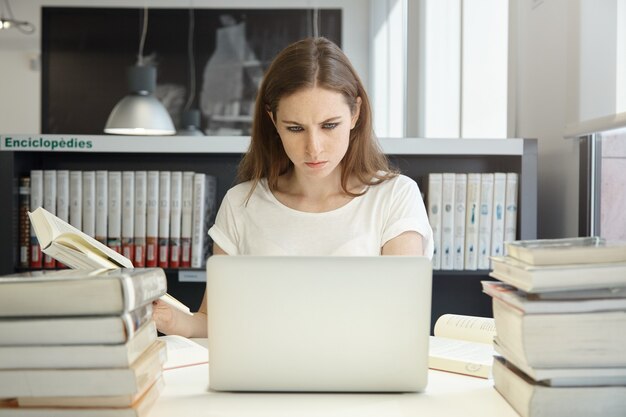 Mujer joven sentada en la biblioteca con un portátil