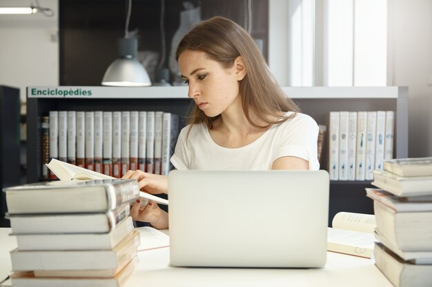 Mujer joven sentada en la biblioteca con un portátil