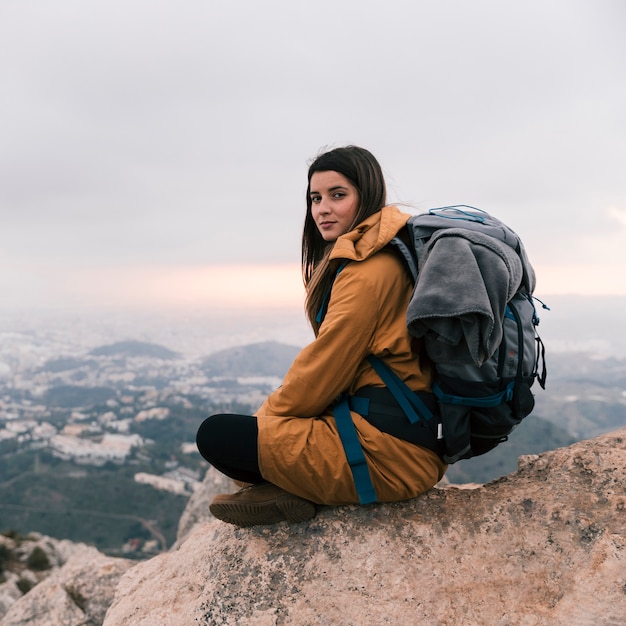 Mujer joven sentada en el borde de la montaña con su mochila