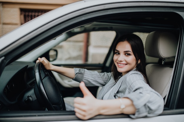 Mujer joven sentada en el coche y mostrando los pulgares para arriba