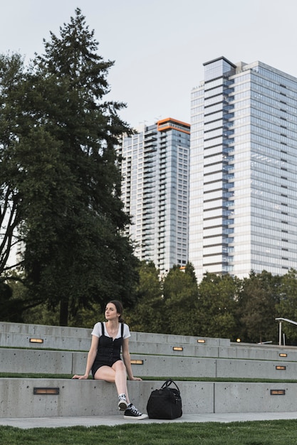 Foto gratuita mujer joven sentada y edificios en el fondo