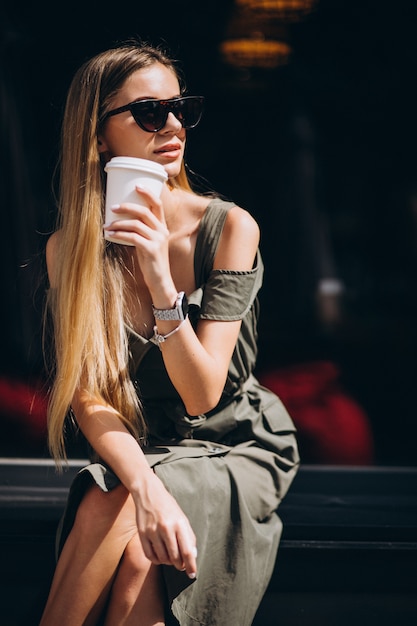 Mujer joven sentada fuera de la cafetería tomando café