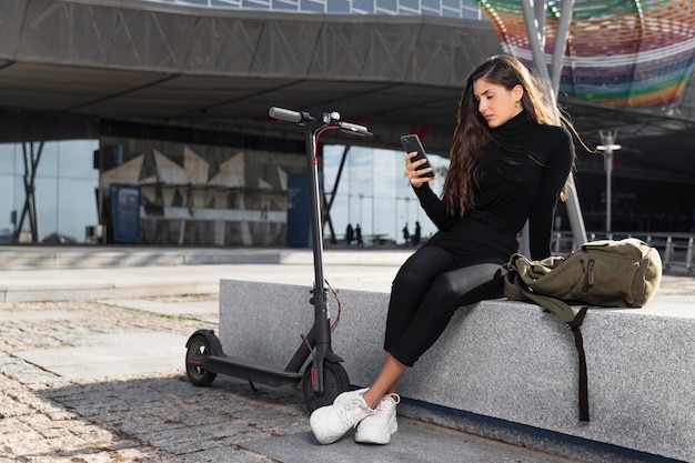 Mujer joven sentada junto a su scooter