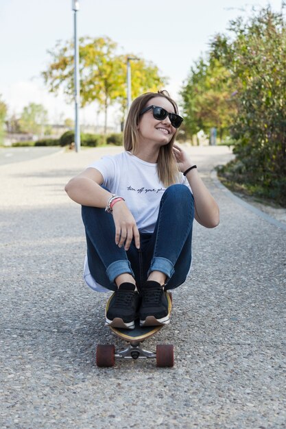 Mujer joven sentada en longboard y sonriendo