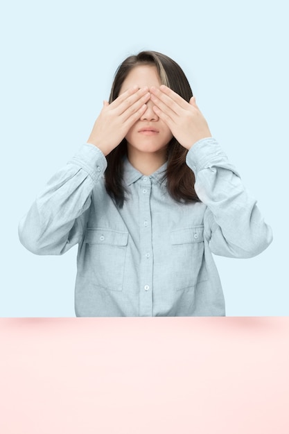 Mujer joven sentada a la mesa en el estudio con los ojos cerrados aislados en azul. no puedo ver nada