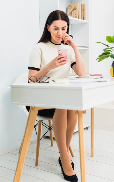 Mujer joven sentada a la mesa con teléfono inteligente