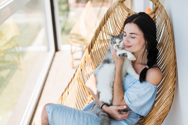 Mujer joven sentada en una silla en el patio amando a su gato mascota