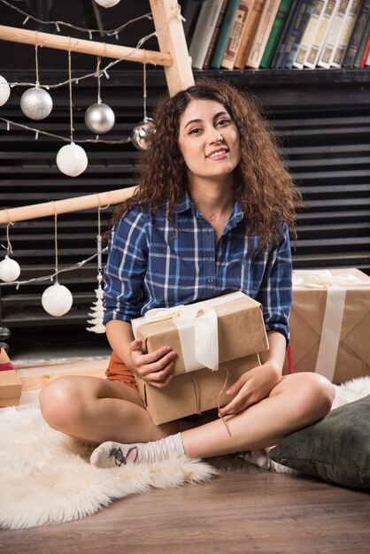 Mujer joven sentada sobre una alfombra mullida con caja de regalo de Navidad