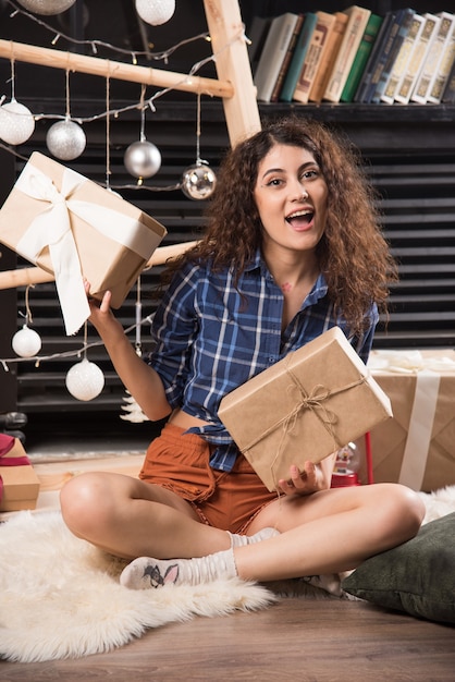 Mujer joven sentada sobre una alfombra mullida con cajas de regalos de Navidad