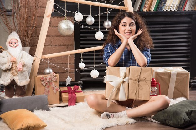 Mujer joven sentada sobre una alfombra mullida con cajas de regalos de Navidad